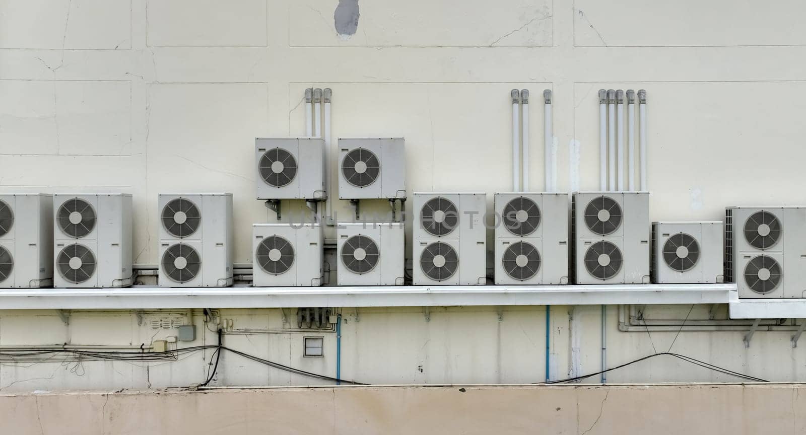 Many condensing units of air conditioners are installed on concrete building wall. Air conditioner maintenance and repair service at home or office. AC maintenance. Air compressor outside building. by Fahroni