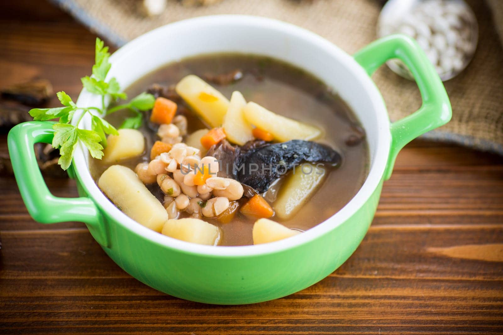 mushroom hot soup with beans in a bowl, on a rustic burlap tablecloth.