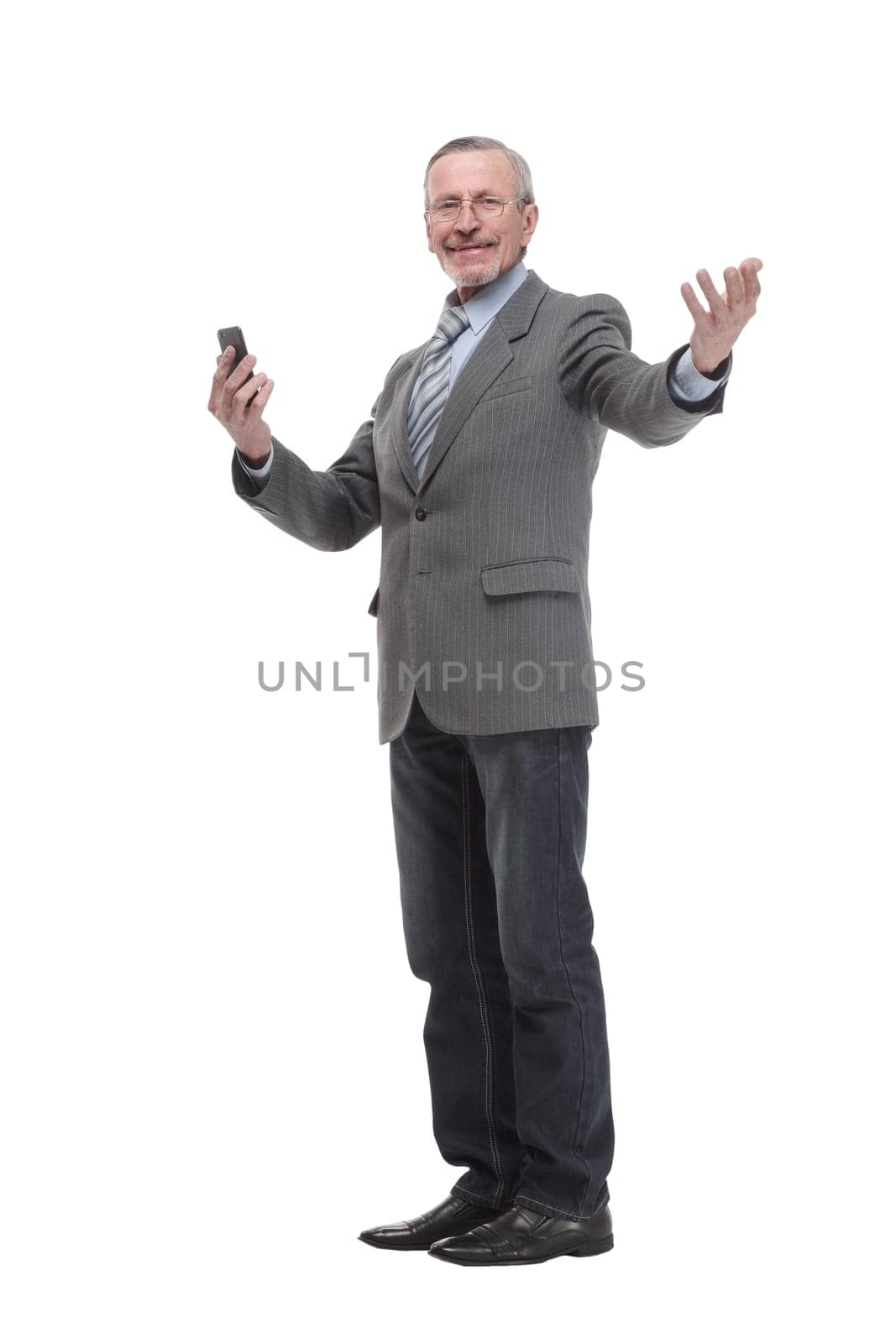 Portrait of a happy mature man dressed in suit holding mobile phone and looking at camera isolated over white background