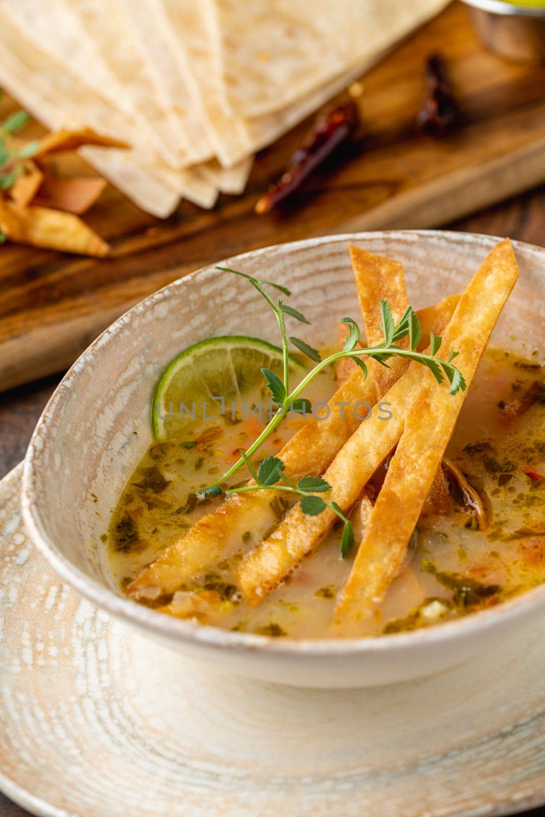 Bowl of tasty Sopa de Lima soup on wooden table by Sonat