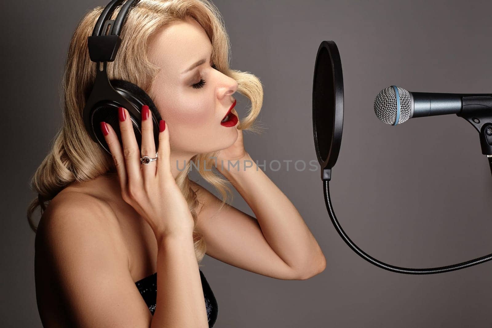 Beautiful Blonde Woman Singing Song in Professional Recording Studio with Microphone, Pop Filter and Headphones. Glamour Pop Diva Creates New Musical Track. Music Karaoke with Female Vocal Artist