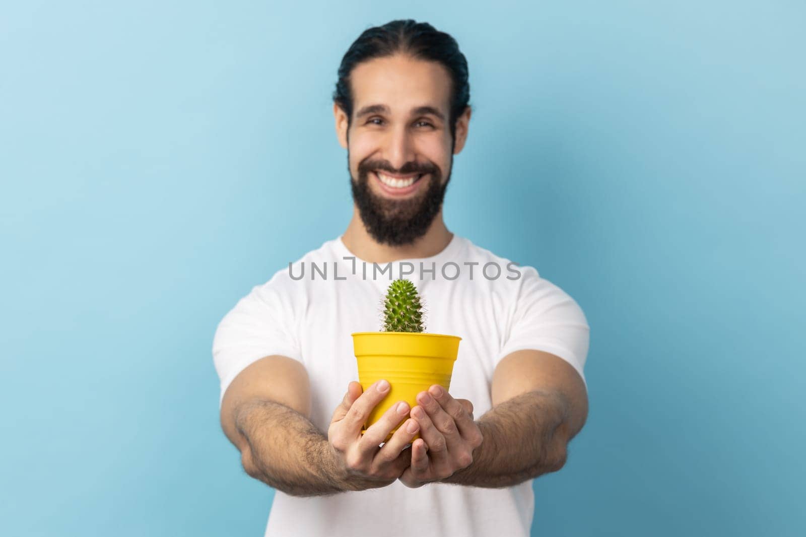 Man holding out flower pot with cactus, looking at camera with toothy smile. by Khosro1