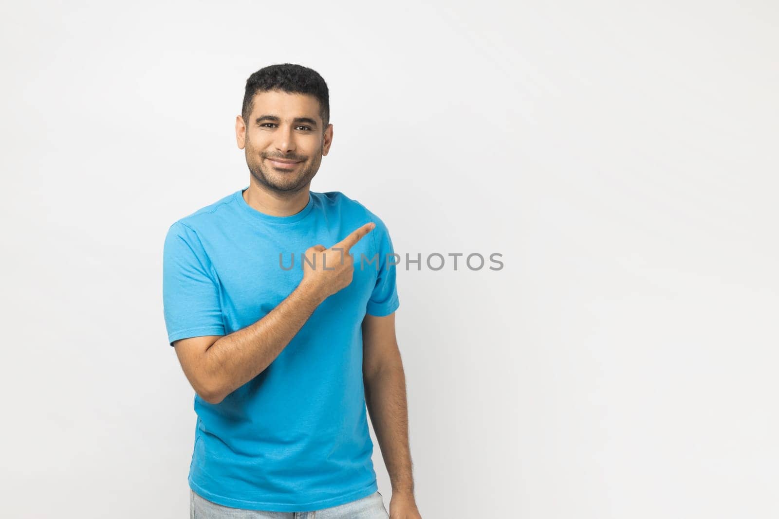 Smiling cheerful attractive unshaven man pointing copy space for advertisement or promotional text. by Khosro1