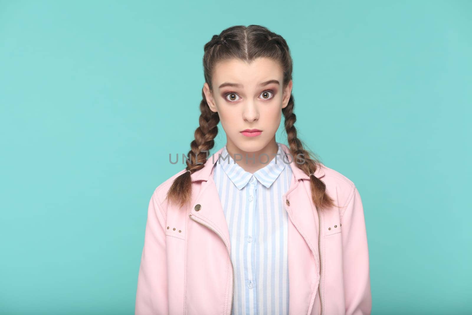 Portrait of shocked surprised teenager girl with braids wearing pink jacket looking at camera with big eyes, being astonished. Indoor studio shot isolated on green background.