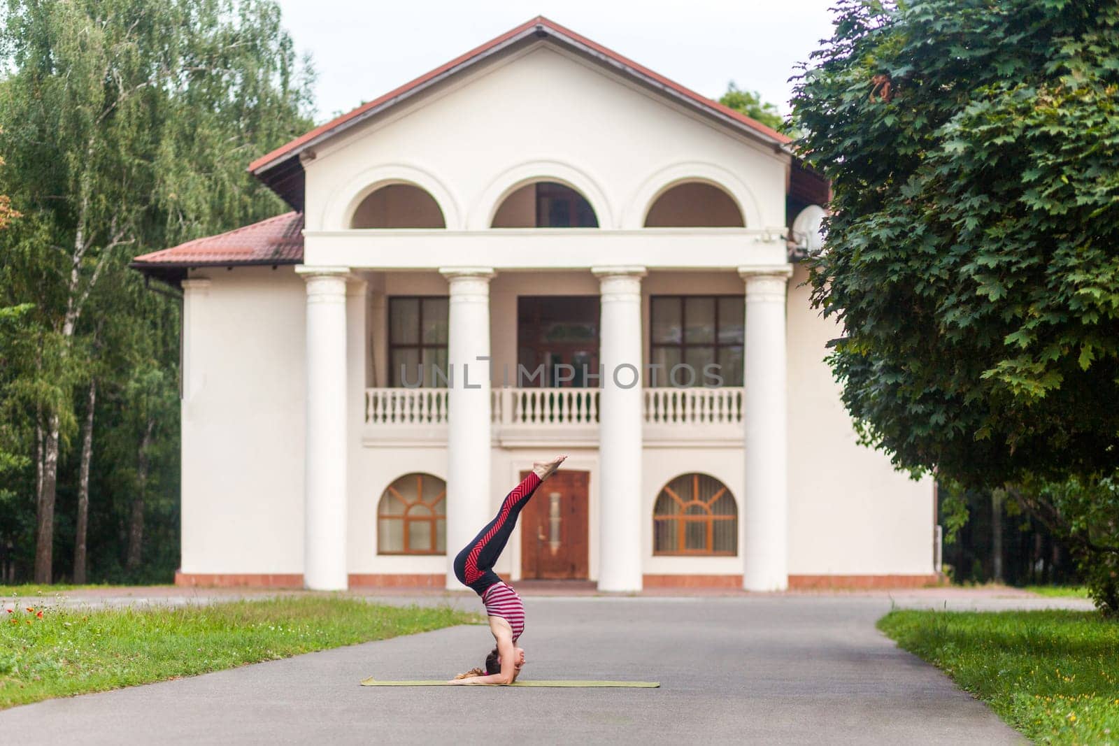 Sporty woman doing yoga asana supported headstand on the street, Salamba Sirsasana, balanced posture by Khosro1