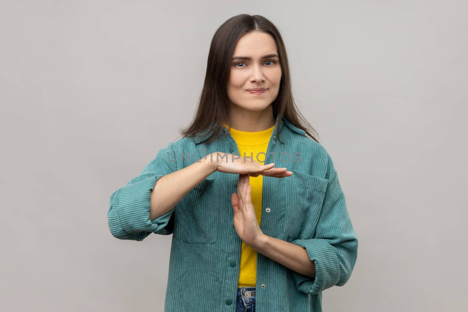 Portrait of stressed young adult woman showing time out gesture, looking with nervous expression, deadline, wearing casual style jacket. Indoor studio shot isolated on gray background.