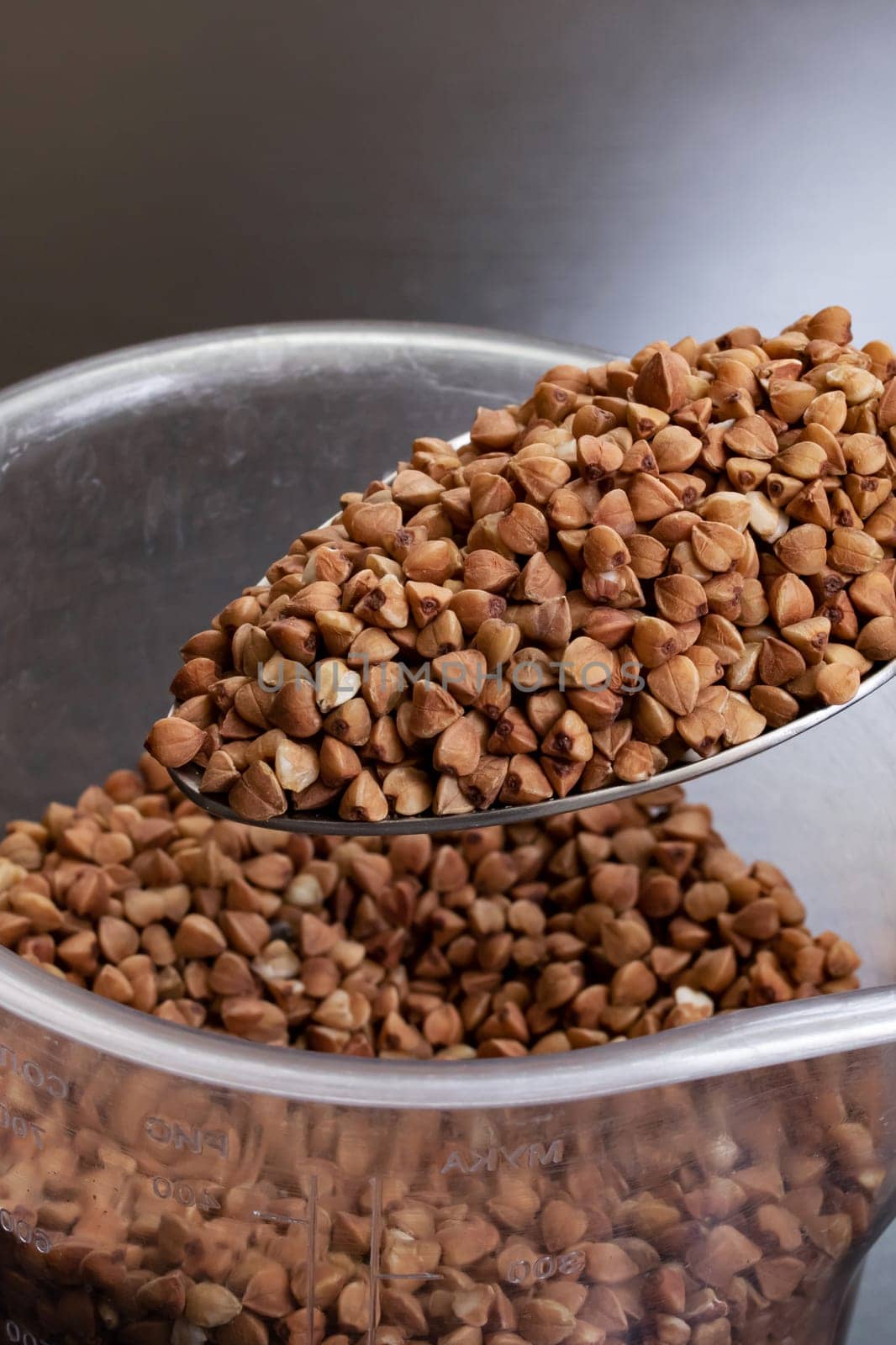 Buckwheat groats in a spoon on black background close up