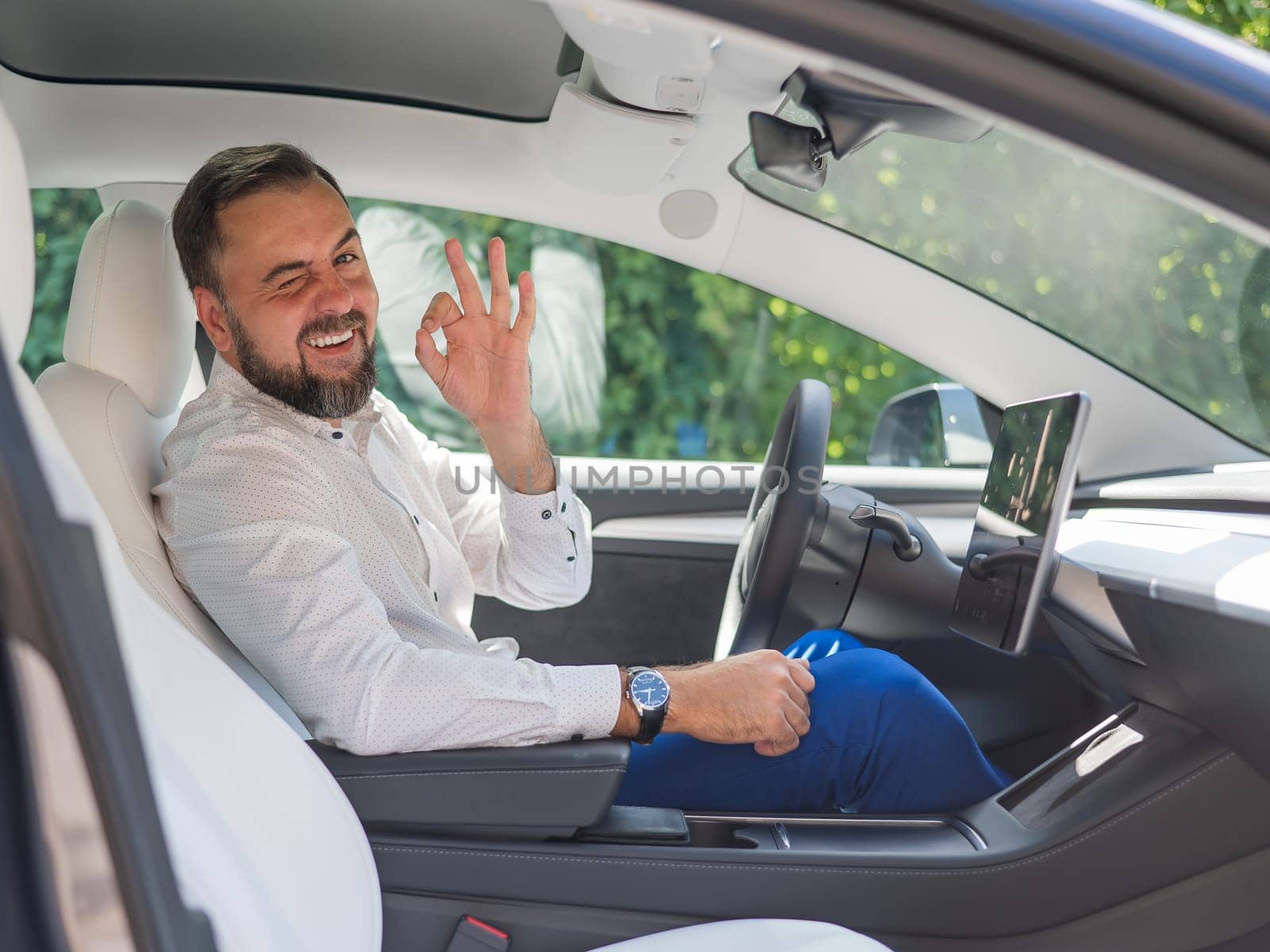 Caucasian bearded man in a suit driving a car shows an ok sign