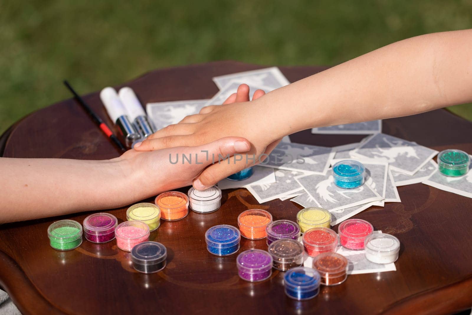 Kid's animator is creating a Shimmering sparkling glitter tattoo on a child's hand at a birthday party. Body art