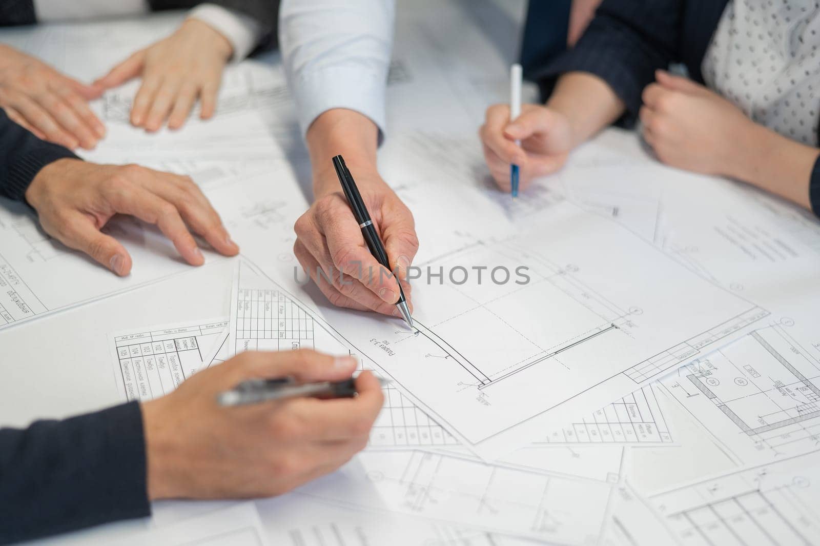 Close-up of the hands of four colleagues with blueprints on the table in the office. Brainstorming of engineers and architects