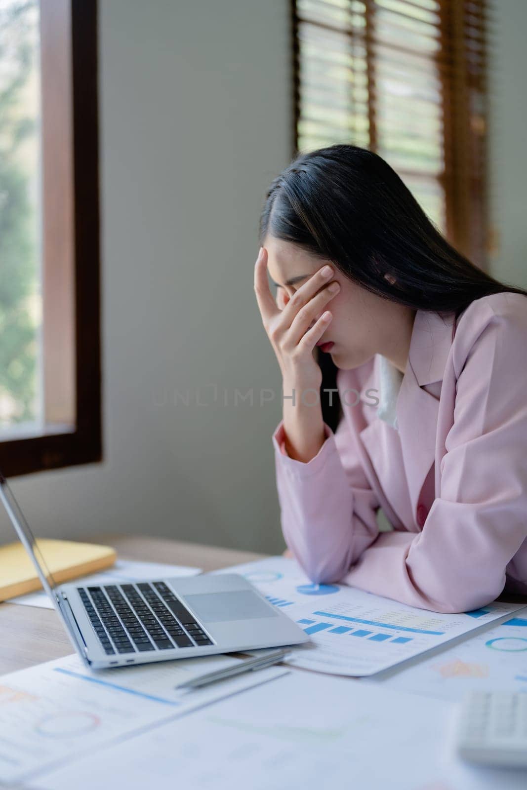 Portrait of a young Asian woman showing acute headache from sitting for a long time at work. by Manastrong