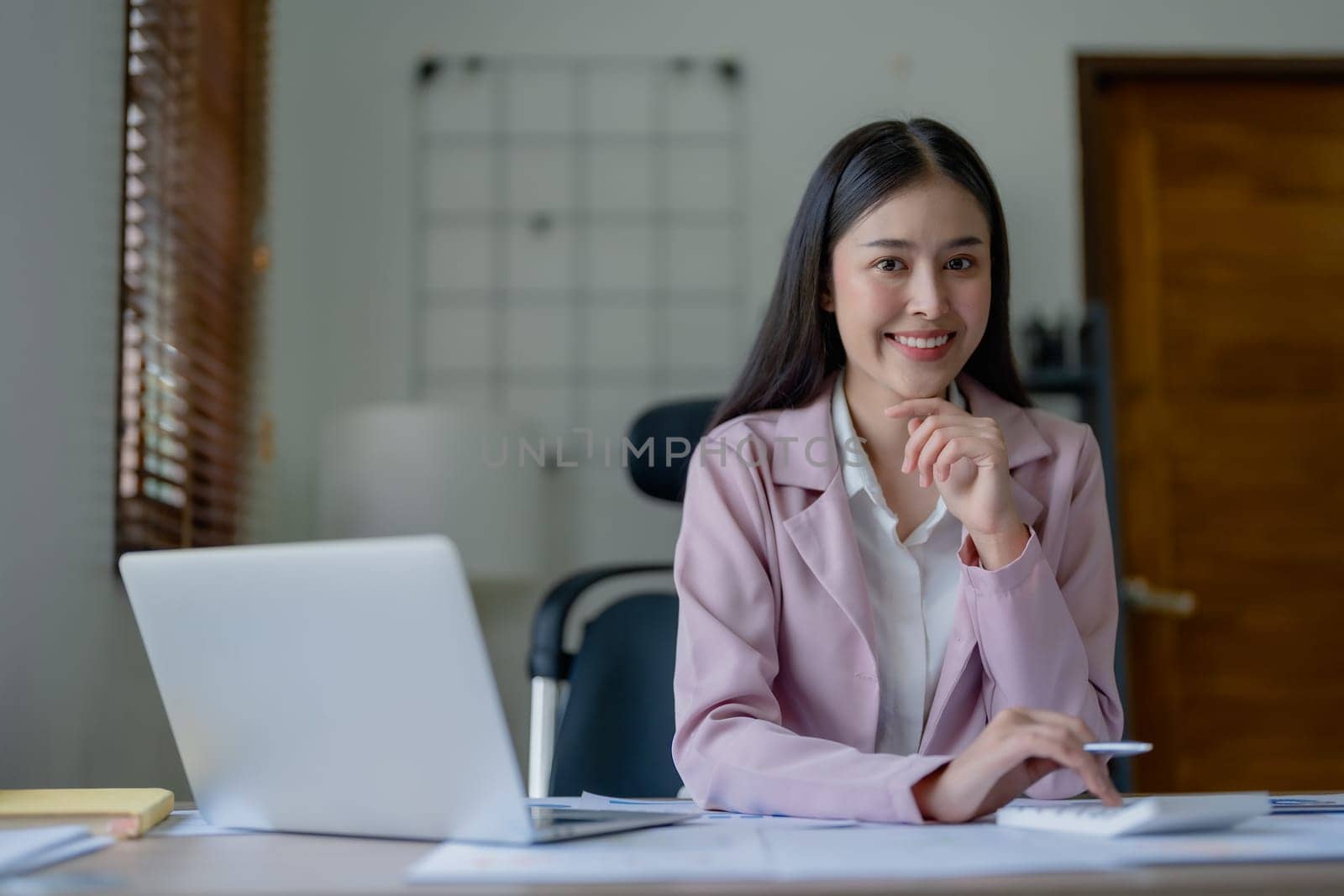 Portrait of a woman business owner showing a happy smiling face as he has successfully invested her business using computers and financial budget documents at work.