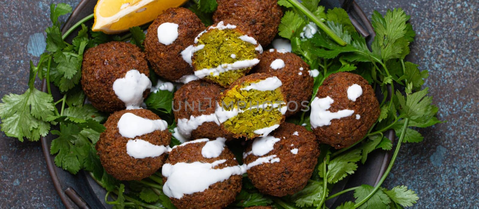 Plate of fried falafel balls served with fresh green cilantro and lemon top view on rustic concrete background. Traditional vegan dish of Middle Eastern cuisine