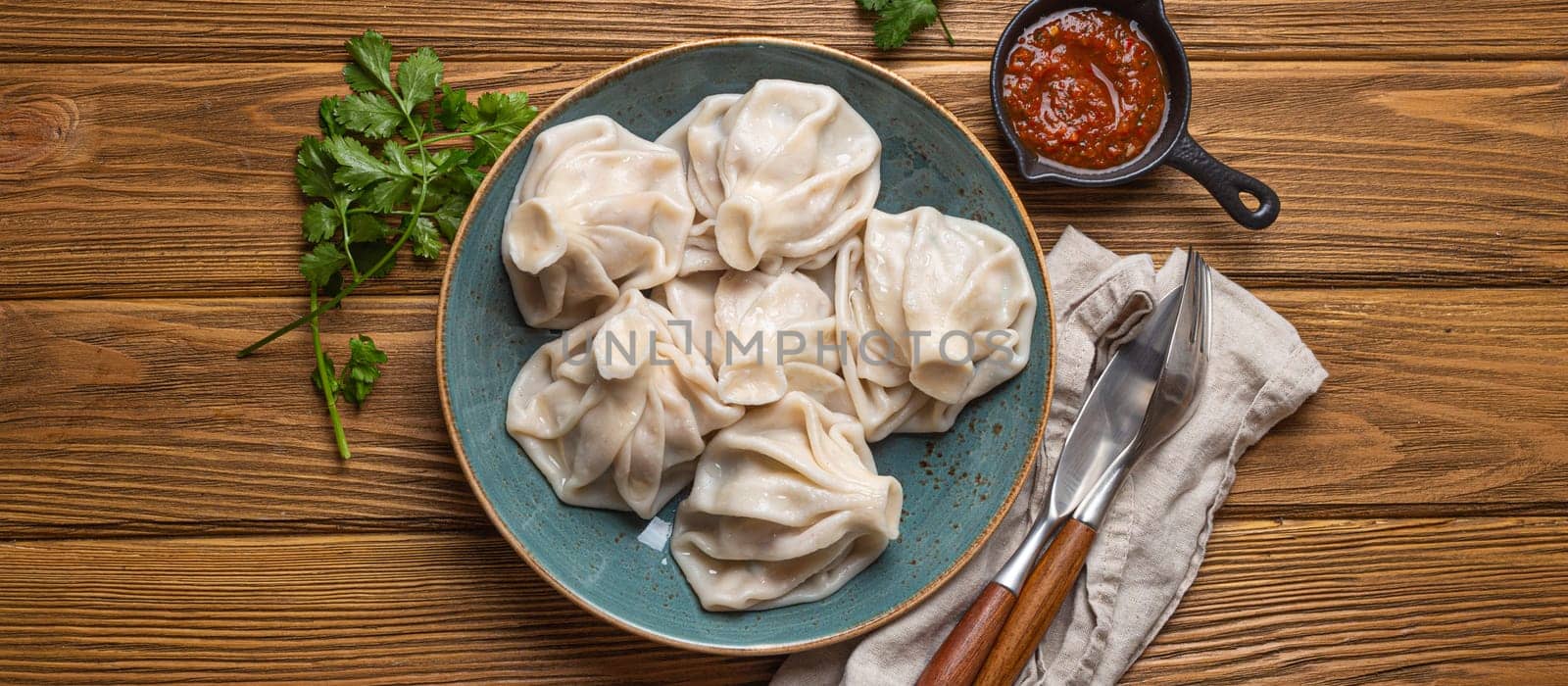 Georgian dumplings Khinkali on plate with red tomato sauce and fresh cilantro top view, rustic wooden background, traditional dish of Georgia by its_al_dente