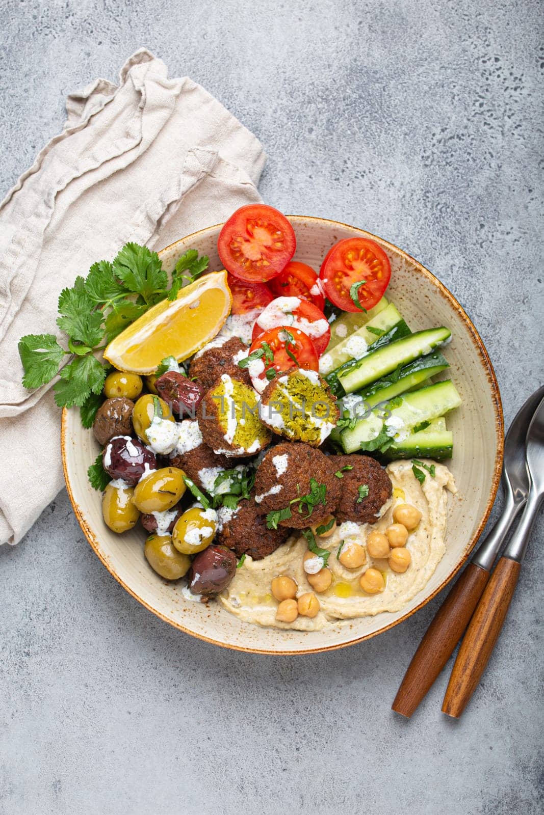 Falafel salad bowl with hummus, vegetables, olives and herbs. Vegan lunch plate top view, rustic stone background, healthy meal with falafel and veggies by its_al_dente