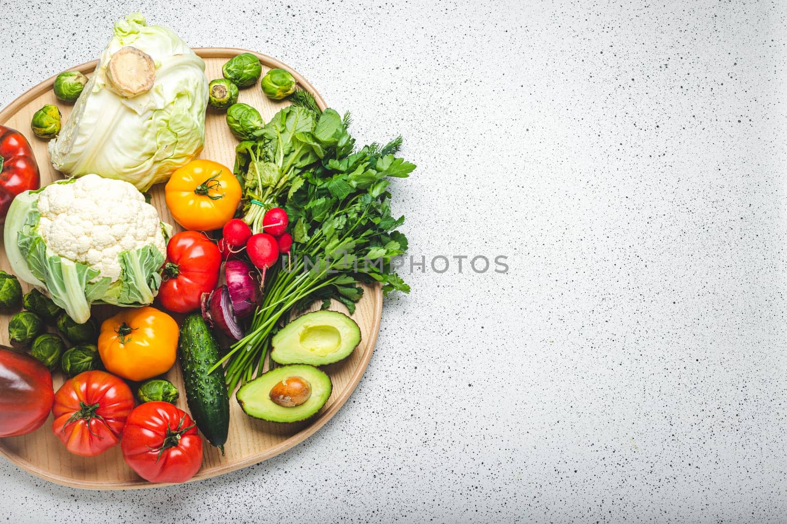 Rustic wooden tray with selection of fresh vegetables and greenery on white kitchen table top view. Vegetarian or diet food from organic ingredients, healthy nutrition concept, space for text