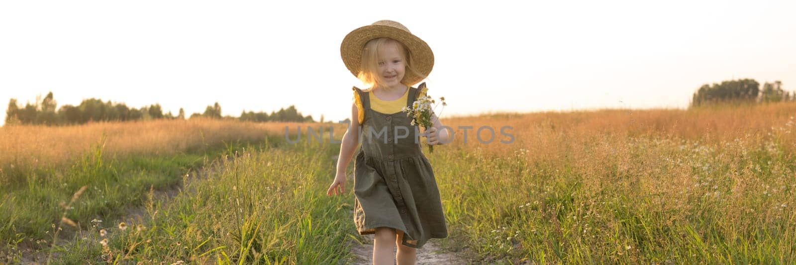 A little blonde girl in a straw hat walks in a field with a bouquet of daisies. The concept of walking in nature, freedom and an eco-friendly lifestyle