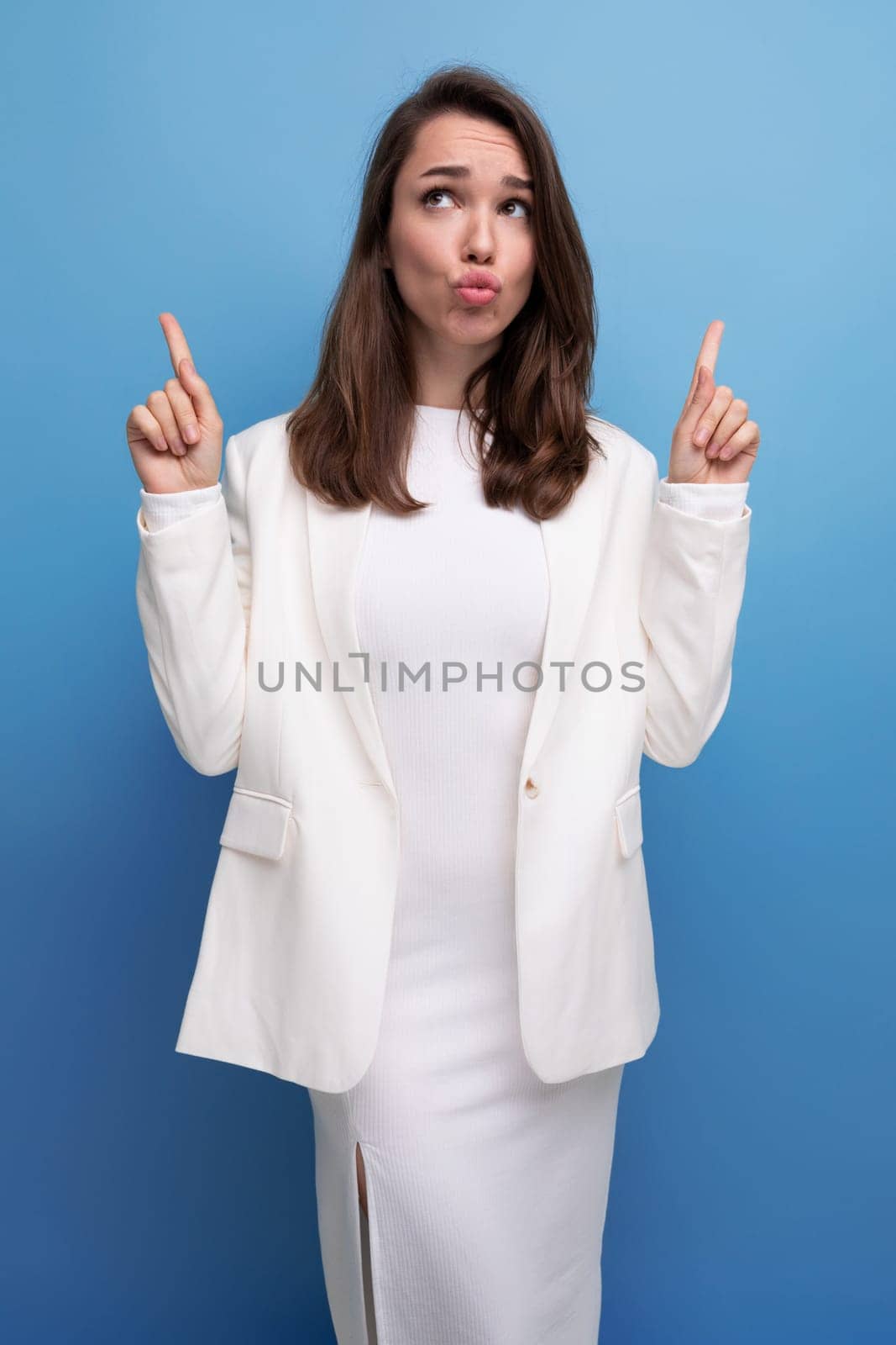 stylish young brunette with long hair woman in white dress points her finger to the side.