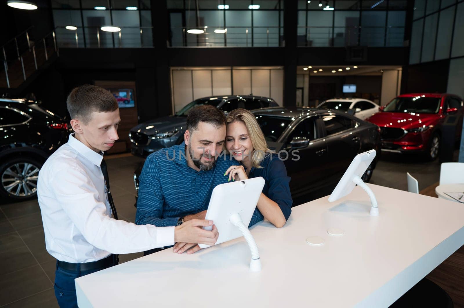 Caucasian married couple chooses a car in a car dealership on digital tablets. by mrwed54