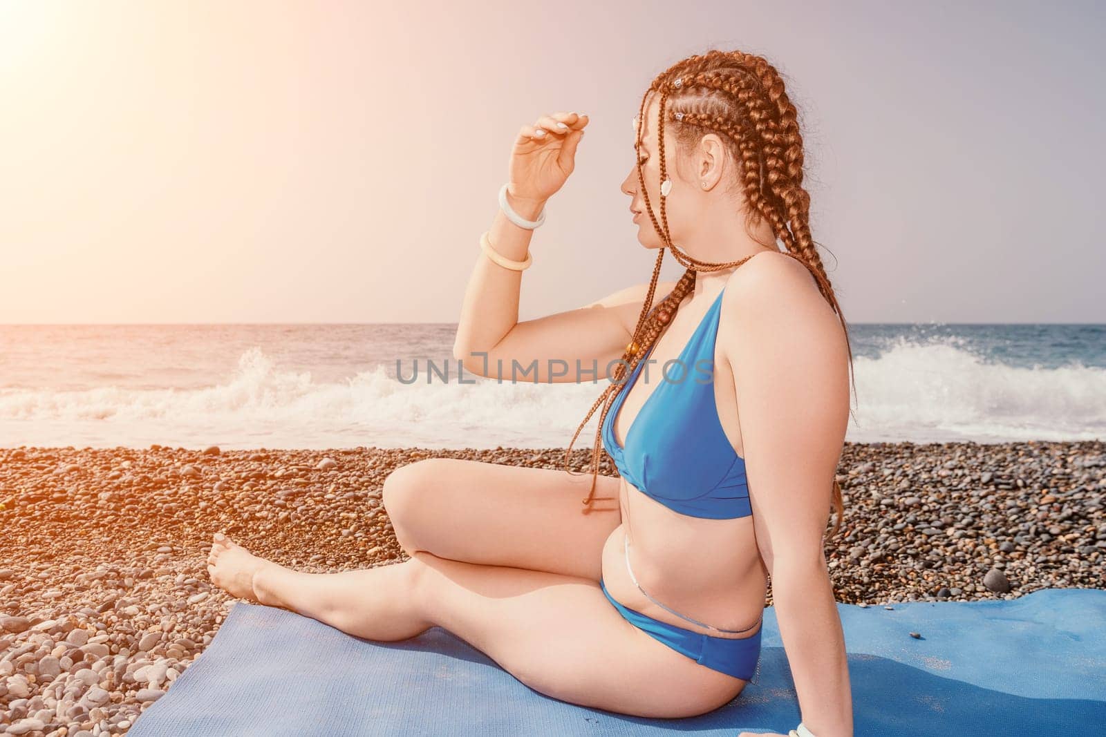 Woman yoga sea. Well looking middle aged woman with braids dreadlocks in white leggings and tops doing stretching pilates on yoga mat near sea. Female fitness yoga routine concept. Healthy lifestyle