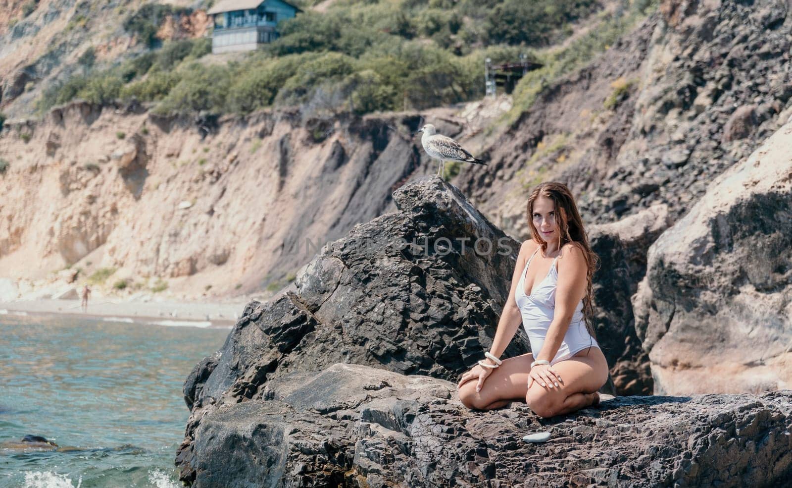 Woman travel sea. Happy tourist in white bikini enjoy taking picture outdoors for memories. Woman traveler posing on the beach at sea surrounded by volcanic mountains, sharing travel adventure journey by panophotograph