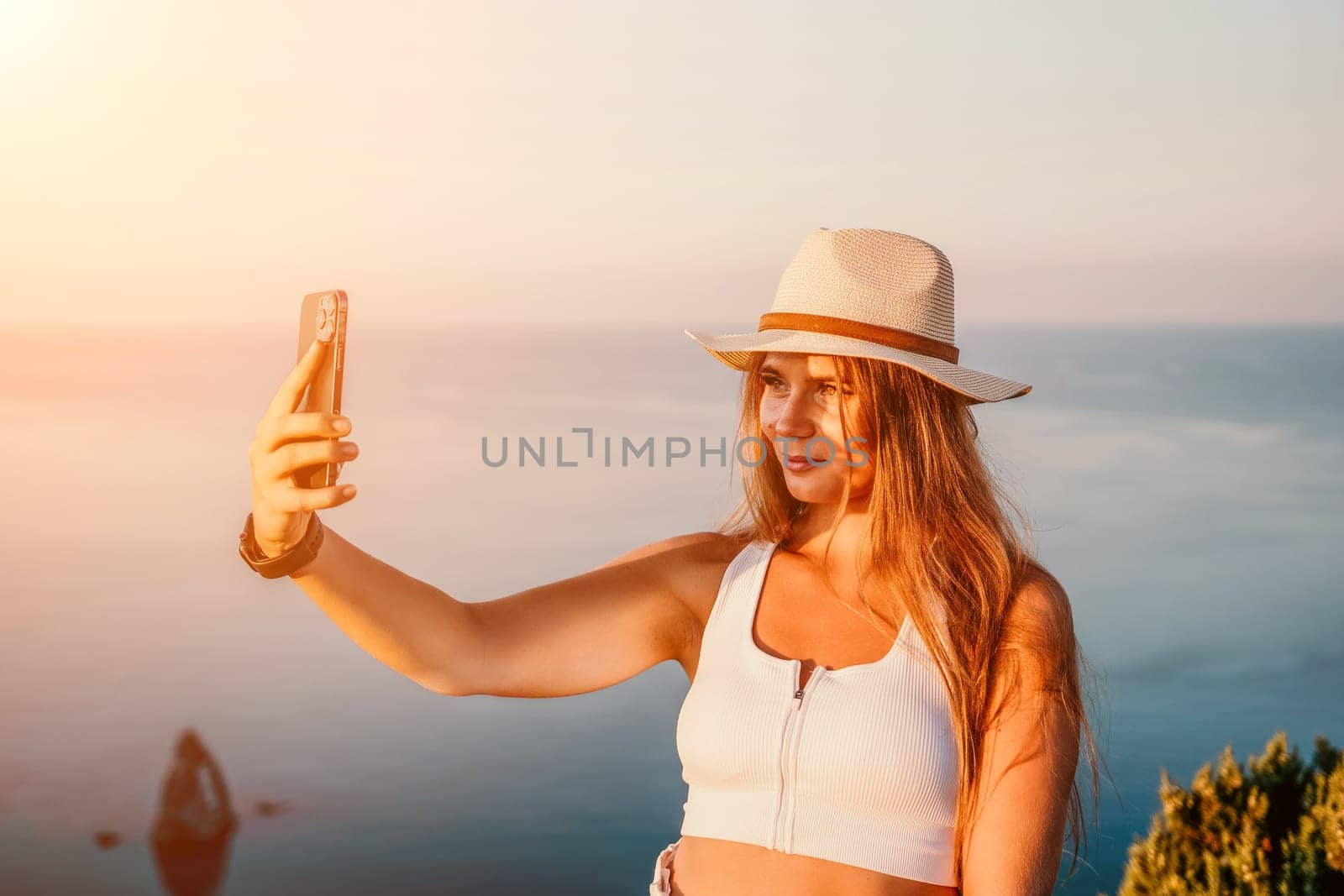 Woman travel sea. Happy tourist in hat enjoy taking picture outdoors for memories. Woman traveler posing on the beach at sea surrounded by volcanic mountains, sharing travel adventure journey