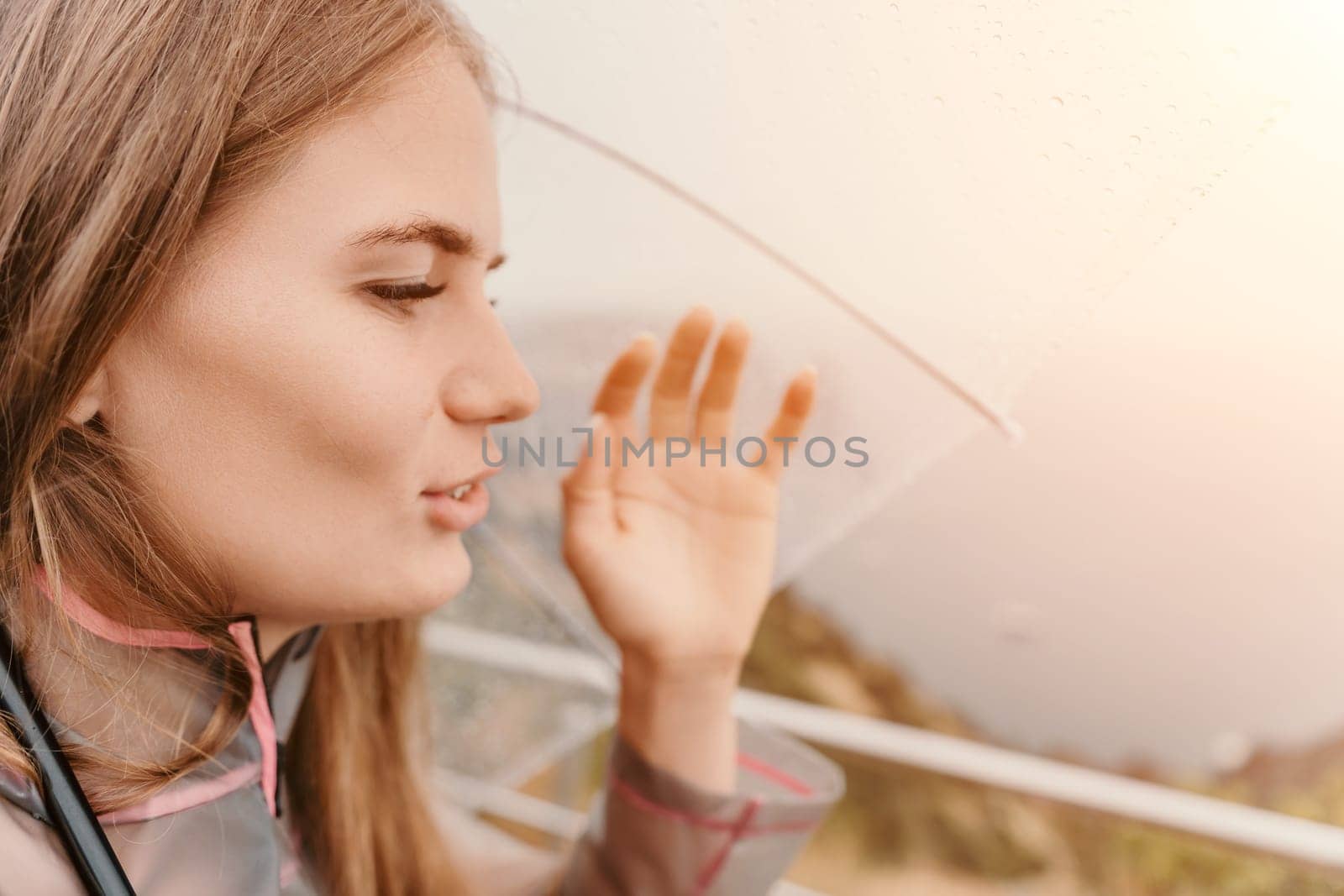 Woman rain park. Happy woman portrait wearing a raincoat with transparent umbrella outdoors on rainy day in park near sea. Girl on the nature on rainy overcast day