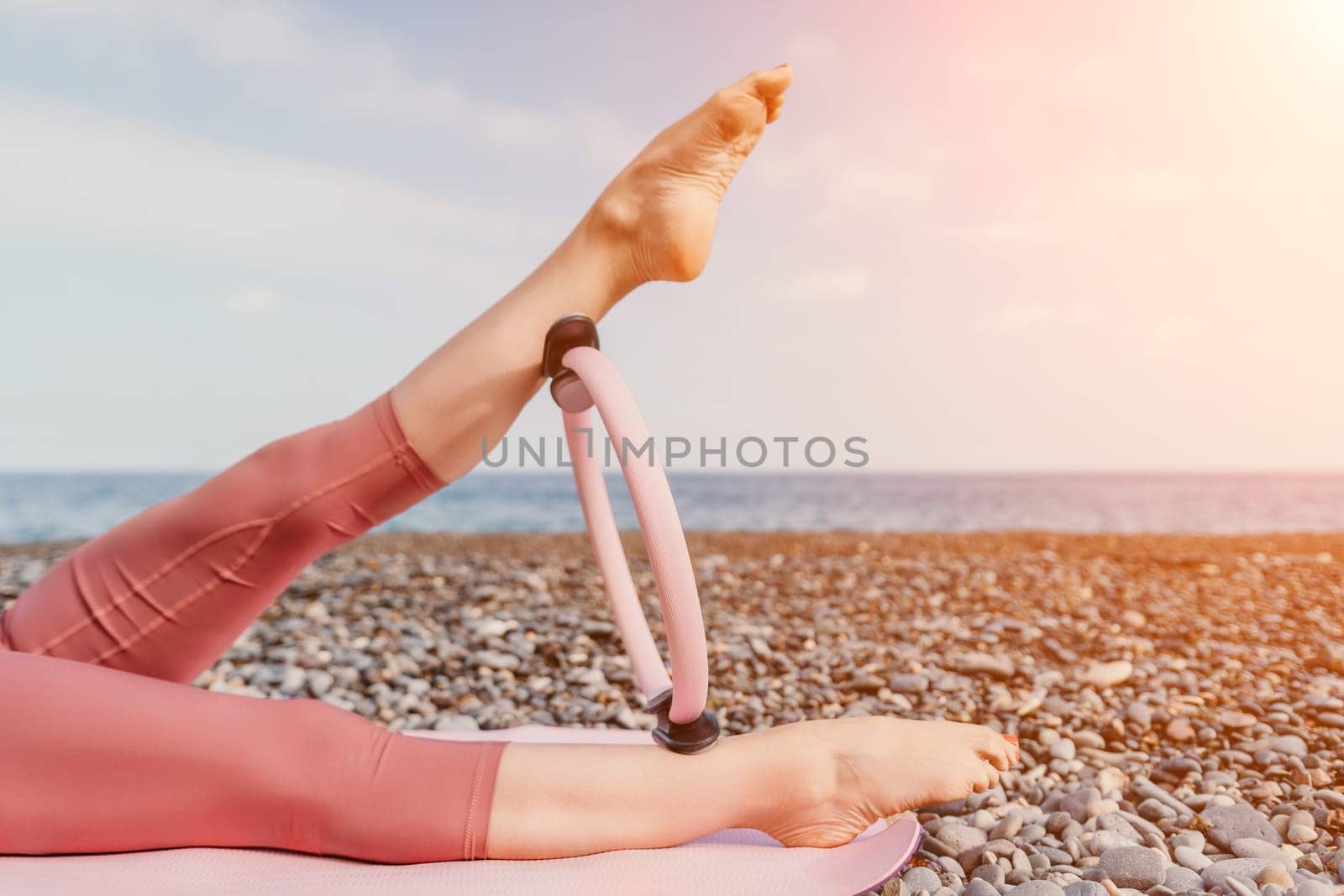 Woman sea pilates. Sporty happy middle aged woman practicing fitness on beach near sea, smiling active female training with ring on yoga mat outside, enjoying healthy lifestyle, harmony and meditation by panophotograph