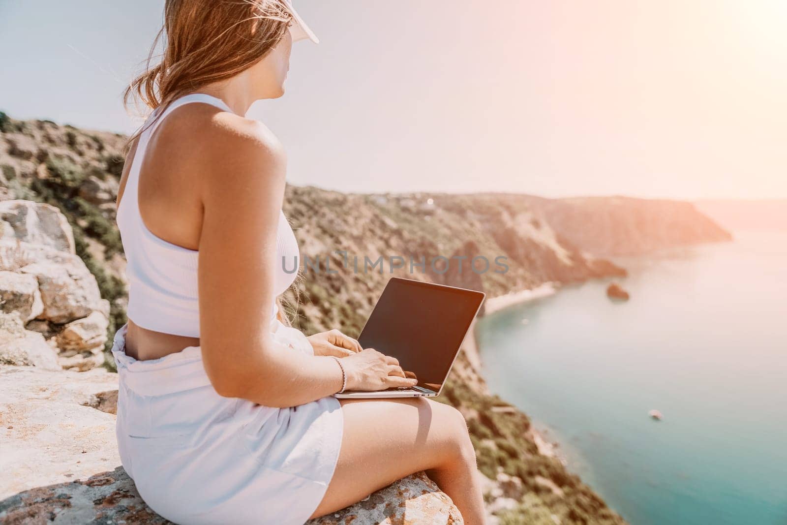 Digital nomad, Business woman working on laptop by the sea. Pretty lady typing on computer by the sea at sunset, makes a business transaction online from a distance. Freelance, remote work on vacation by panophotograph