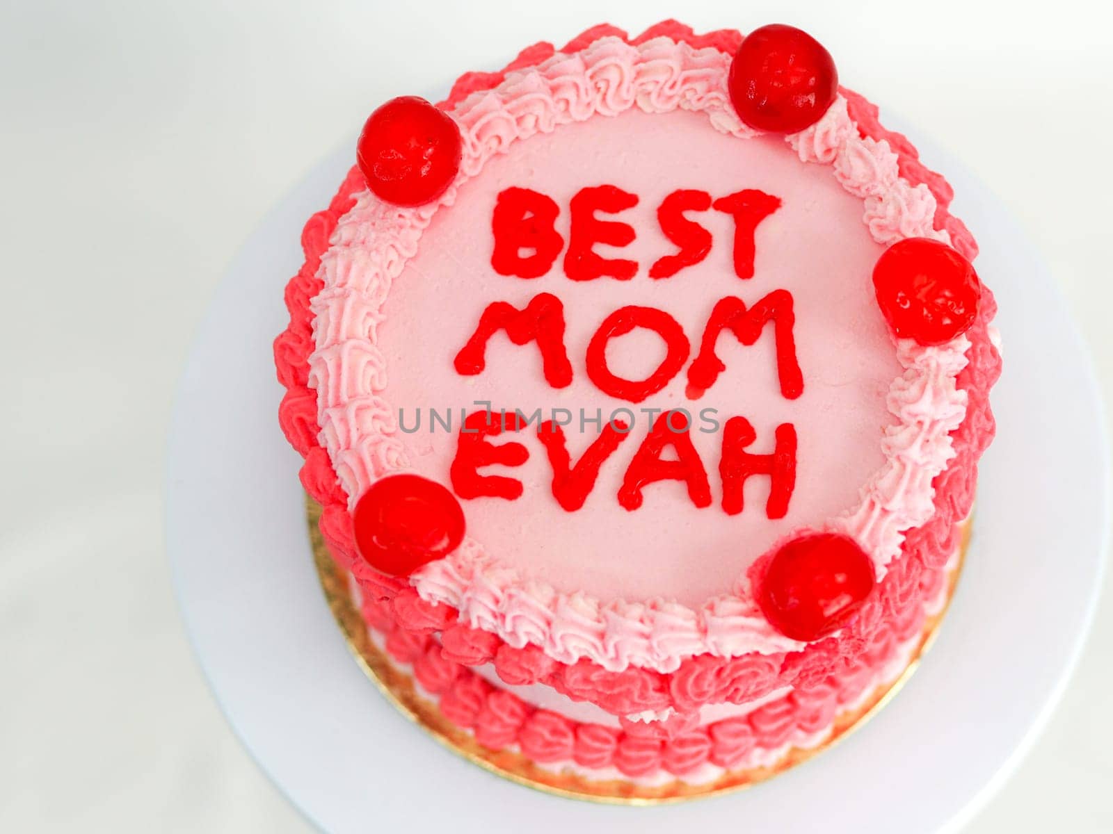 frosted pink red cake for mothers day celebration with funny text topping best mom evah on white studio background