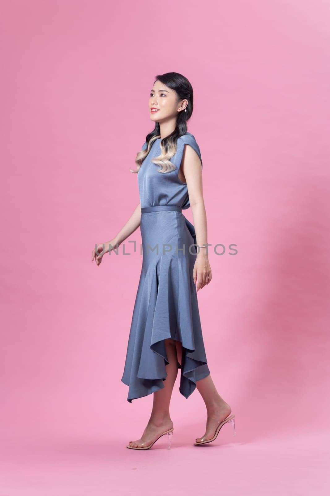 Pretty stylish girl with long curly hair wearing beautiful blue dress and posing against pink background by makidotvn