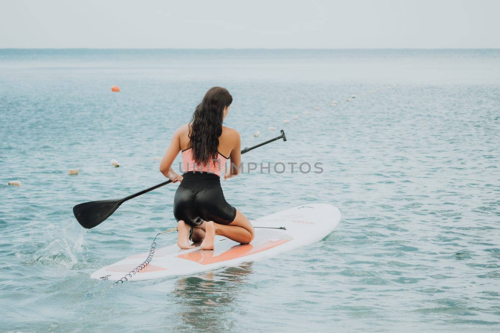 Sea woman sup. Silhouette of happy young woman in pink bikini, surfing on SUP board, confident paddling through water surface. Idyllic sunset. Active lifestyle at sea or river. Slow motion