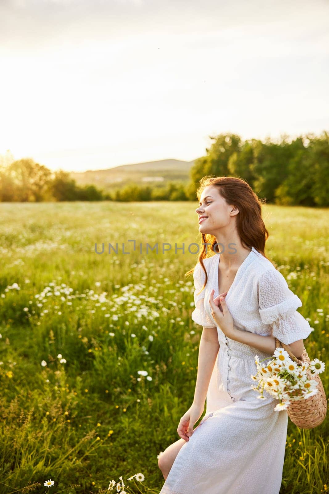 vertical portrait of a beautiful woman in a light dress with a basket full of daisies in nature by Vichizh