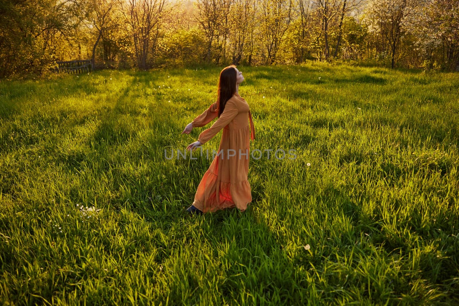 a joyful woman runs through a green field with her hands behind her back, enjoying a warm summer day and nature during the sunset. Horizontal photography in nature. High quality photo