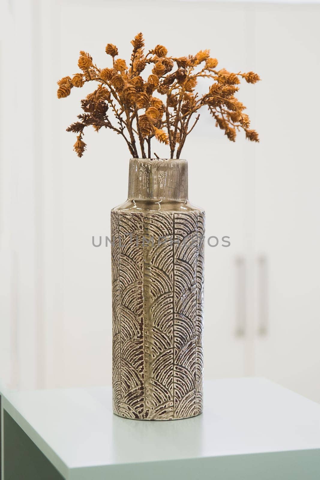 Decorative brown vase with dried plants in a bright interior.