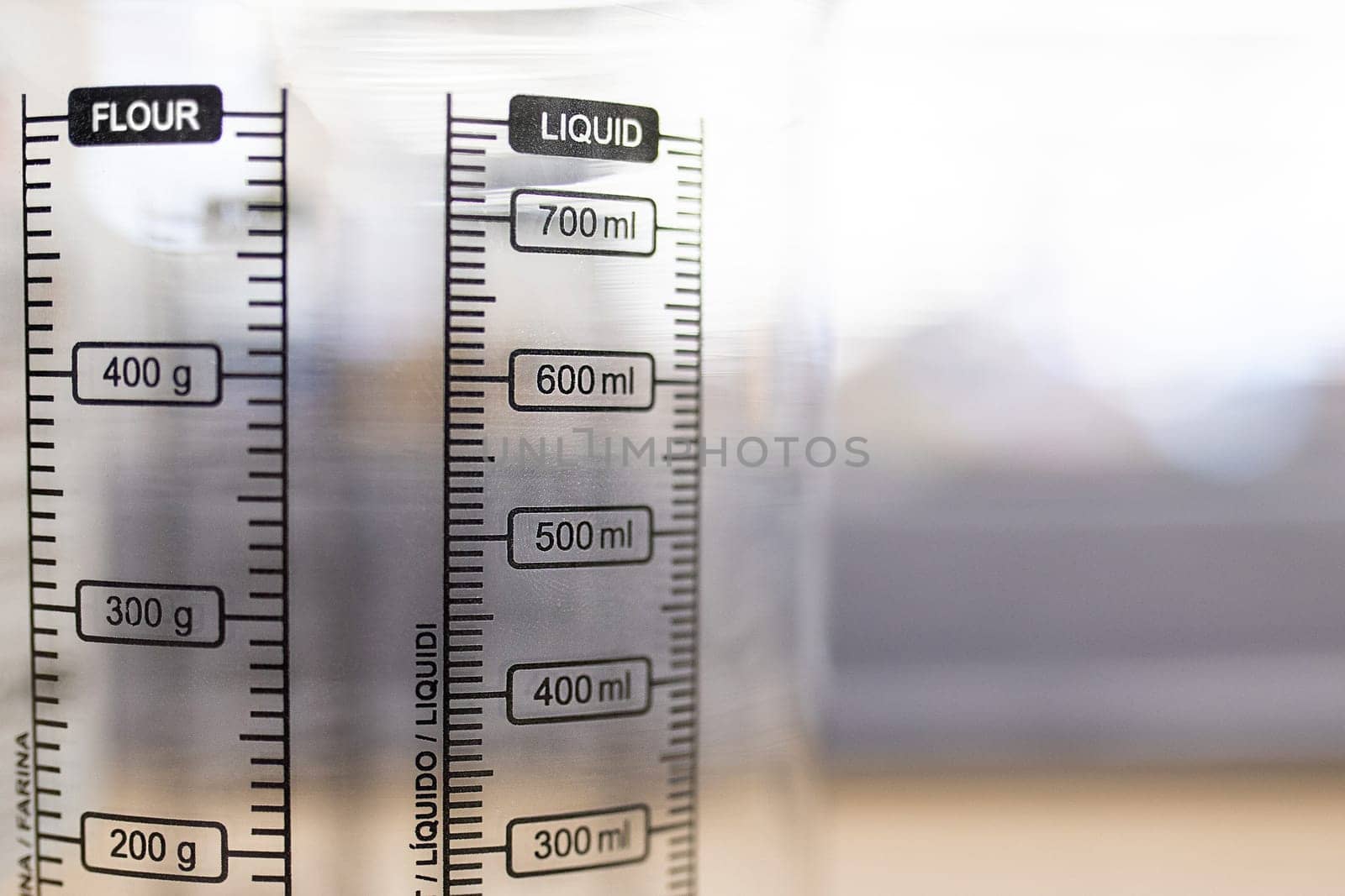 Close-up on a transparent measuring jug with scales for flour and liquid, selective soft focus.