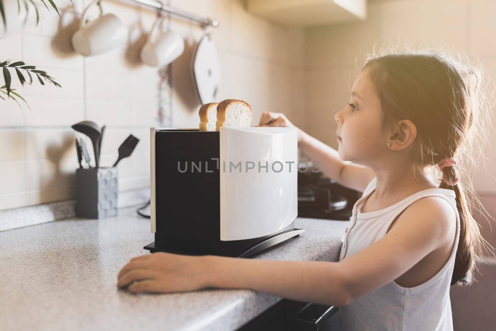 5 - 7 year old kid girl who is preparing breakfast from toast in a toaster in cozy home interior, selective soft focus.