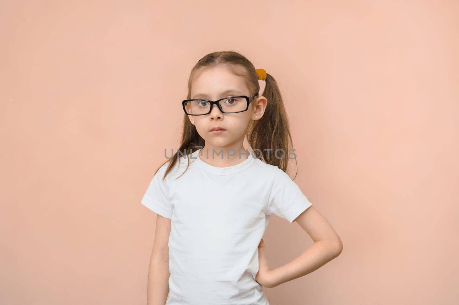 Portrait of a girl of elementary school age in rectangular optical glasses on a pink background.