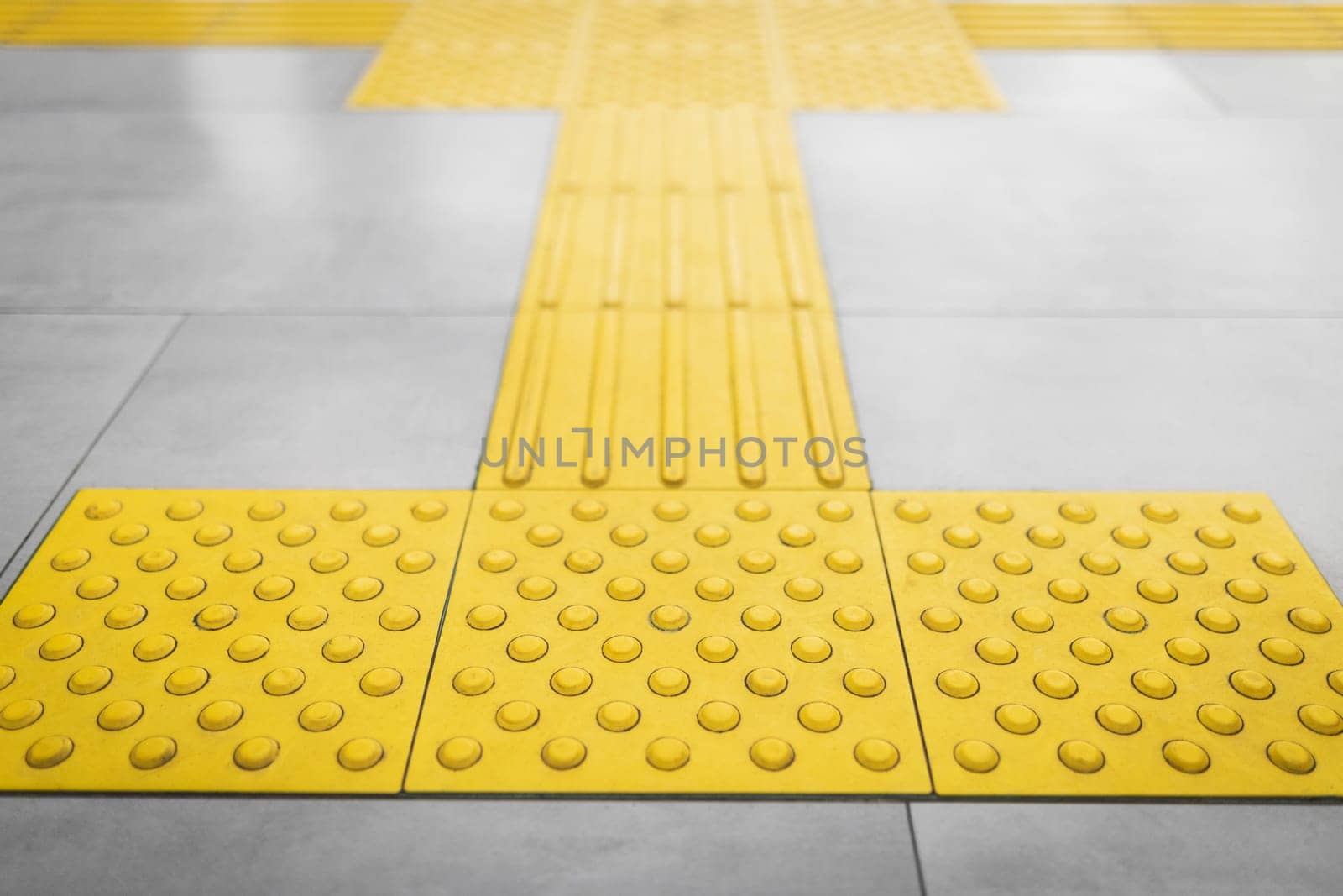 Top view of yellow tactile tiles for the blind stacked on gray tiled floor.