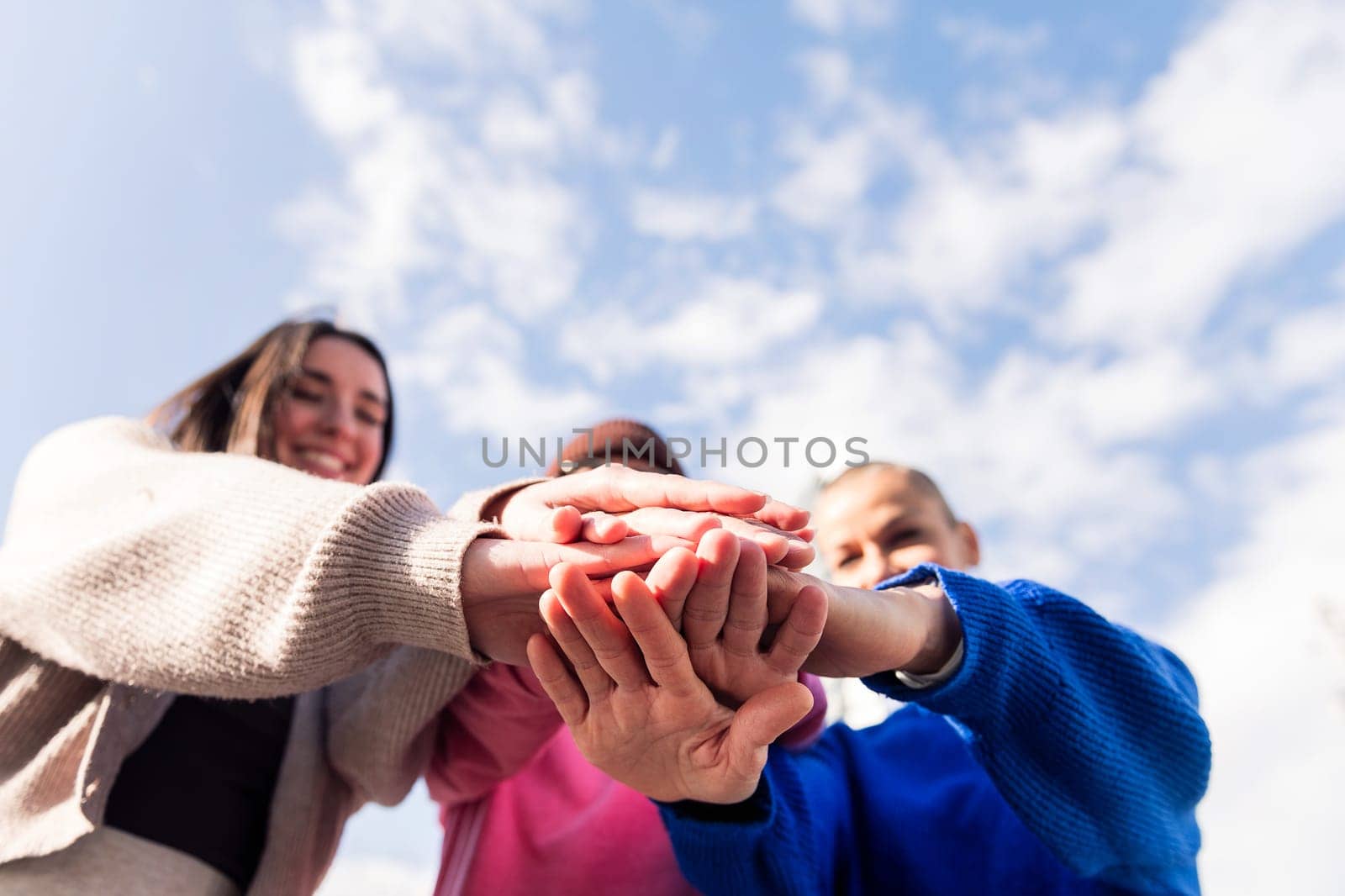 three happy friends holding hands in unity with copy space for text, focus on hands, concept of friendship and bonding