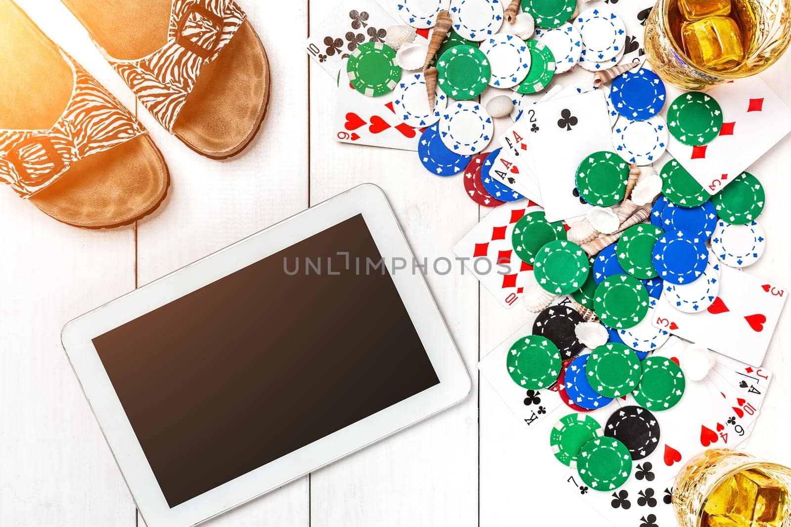 Gambling. Poker chips, cards and the dice nearby tablet on white wooden table. Top view. Copyspace. Poker. Summer. Sun flare