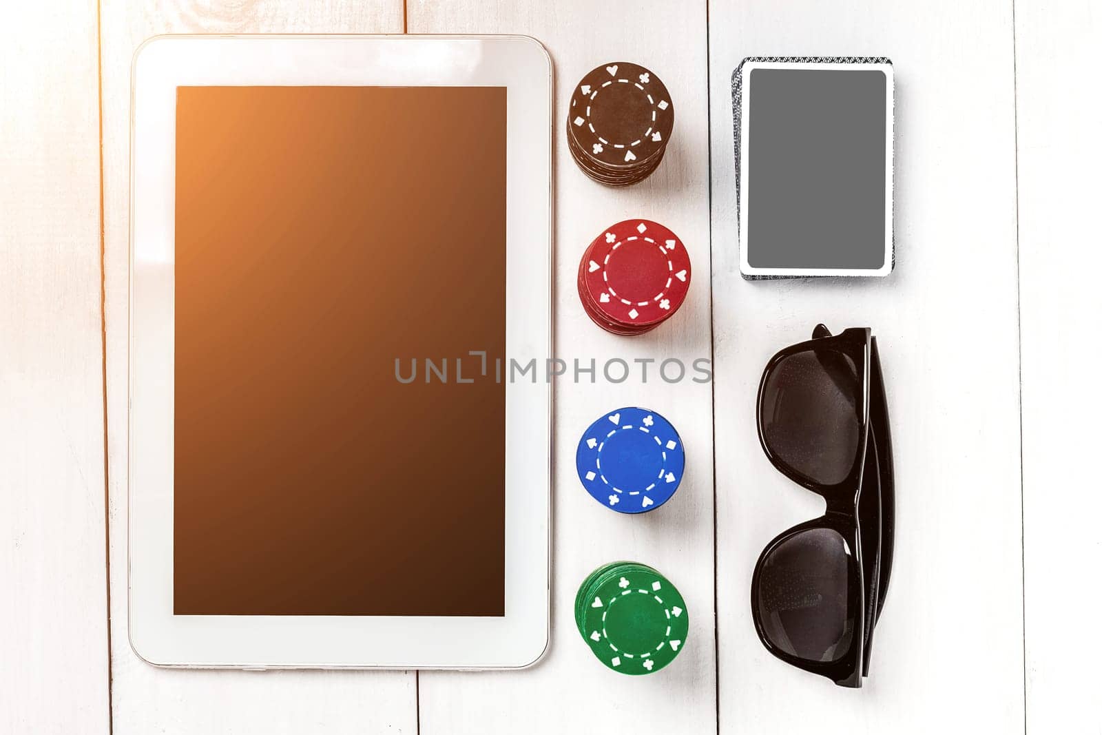 Gambling. Poker chips, cards and the dice nearby tablet on white wooden table. Top view. Copyspace. Poker. Summer. Sun flare