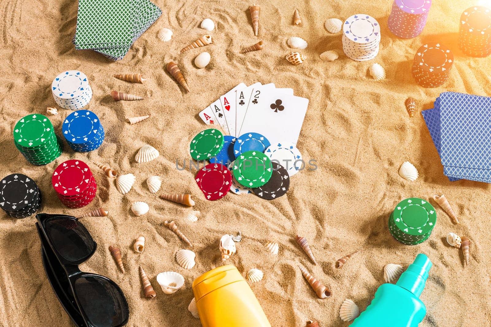 Gambling on vacation concept - white sand with seashells , colored poker chips and cards. Top view. Copy space. Summer. Sun flare