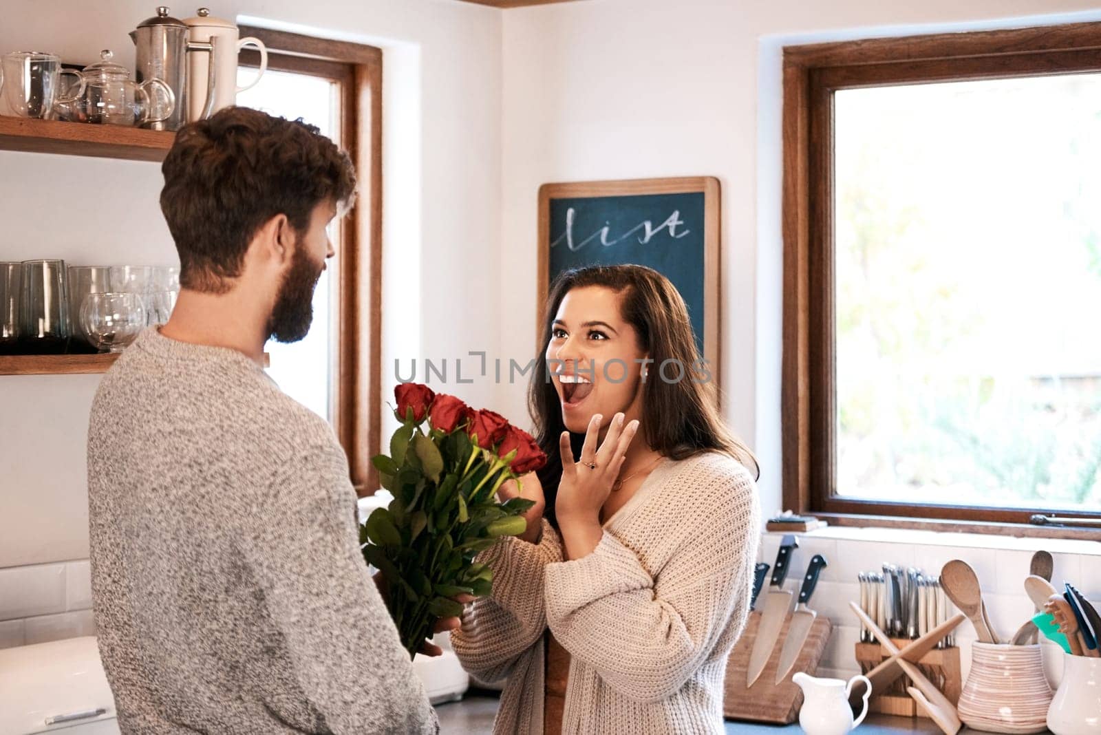 Romance keeping the horticulture industry alive. a young man surprising his wife with a bunch of roses at home. by YuriArcurs