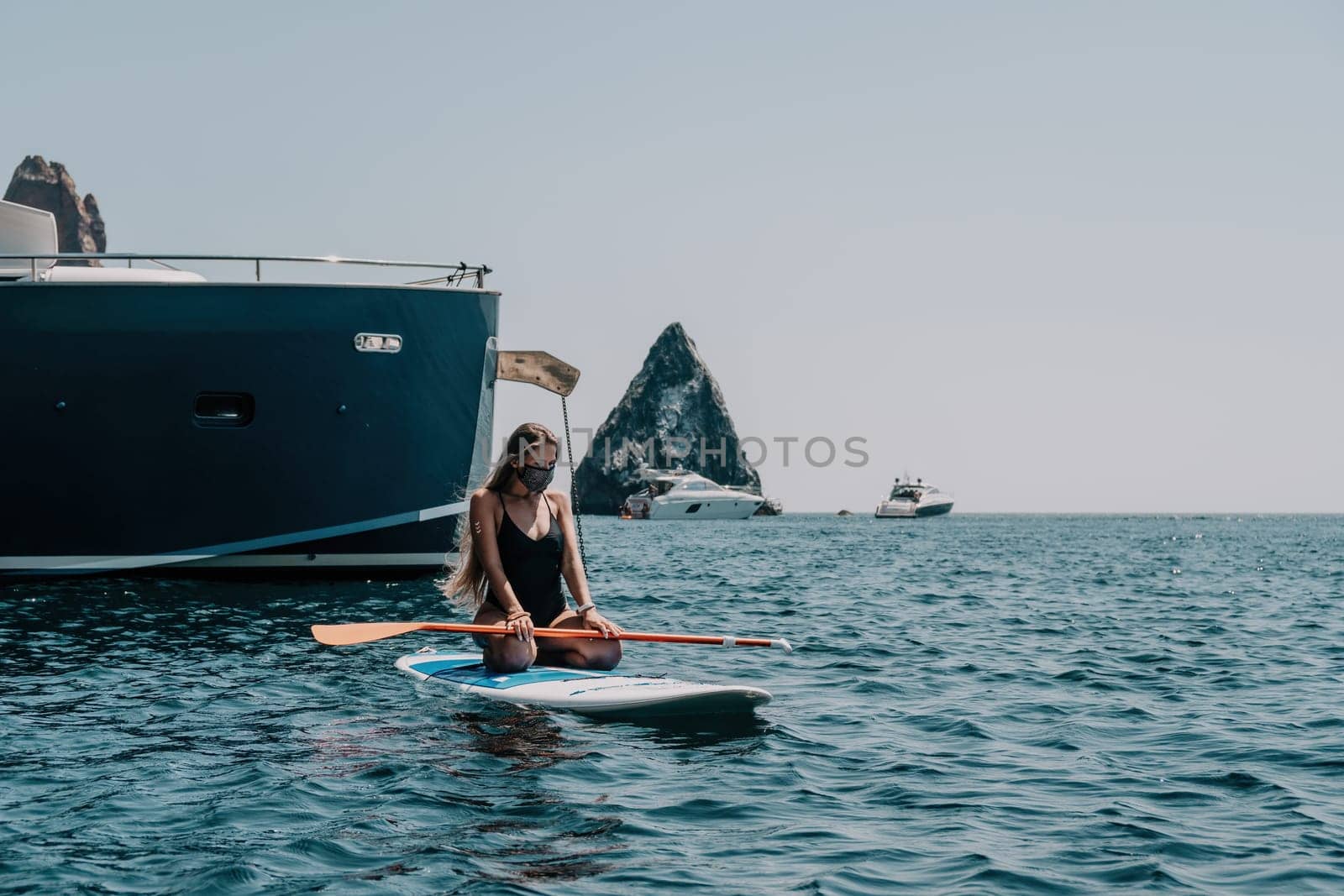 Close up shot of beautiful young caucasian woman with black hair and freckles looking at camera and smiling. Cute woman portrait in a pink bikini posing on a volcanic rock high above the sea