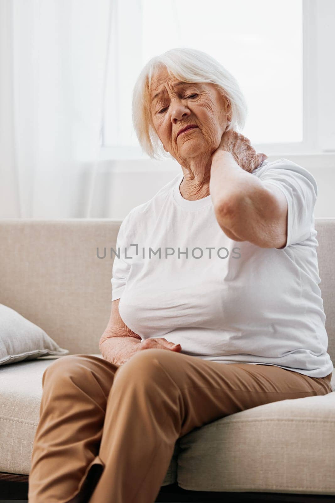 Elderly woman severe neck pain sitting on the sofa, health problems in old age, poor quality of life. High quality photo