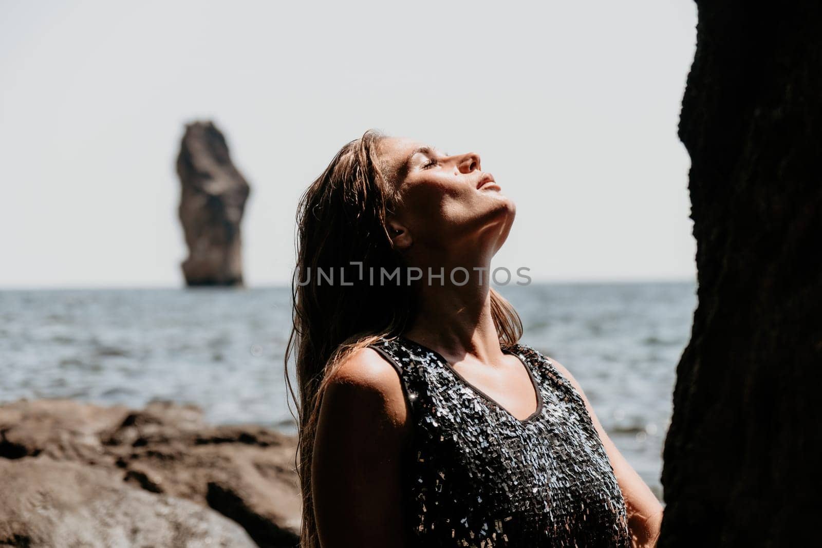 Woman travel sea. Young Happy woman in a long red dress posing on a beach near the sea on background of volcanic rocks, like in Iceland, sharing travel adventure journey