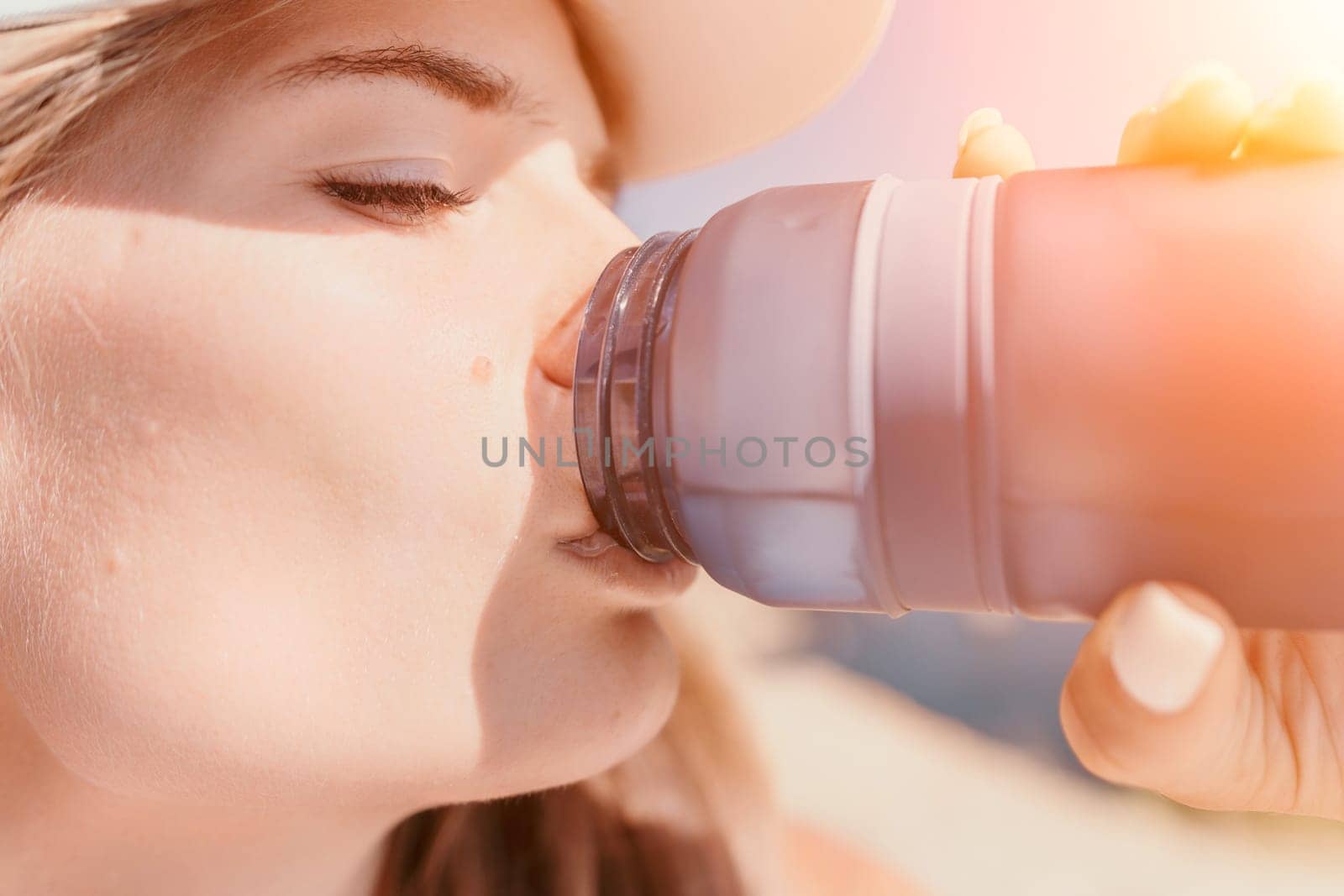 Fintess woman drinking water. Happy, active middle aged woman standing on beach and drinking water after excersise. Concept of lifestyle, sport. Close up.