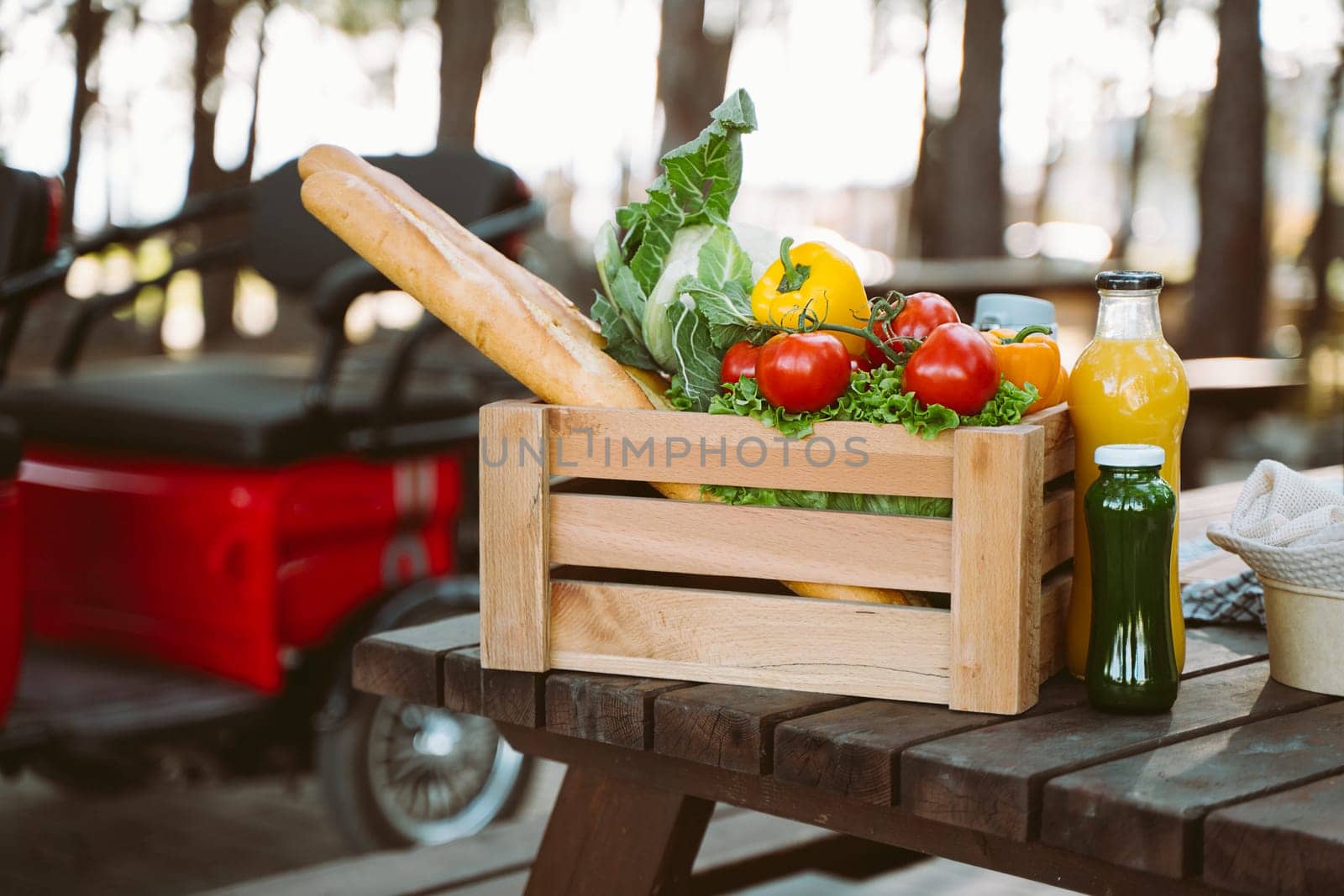 Wooden crate organic farmland vegetables, bread baguettes, fruits, multicolor juice bottles on table electric tricycle background. Framed box cauliflower, sweet pepper, tomatoes, yellow quince, apple. by Ostanina
