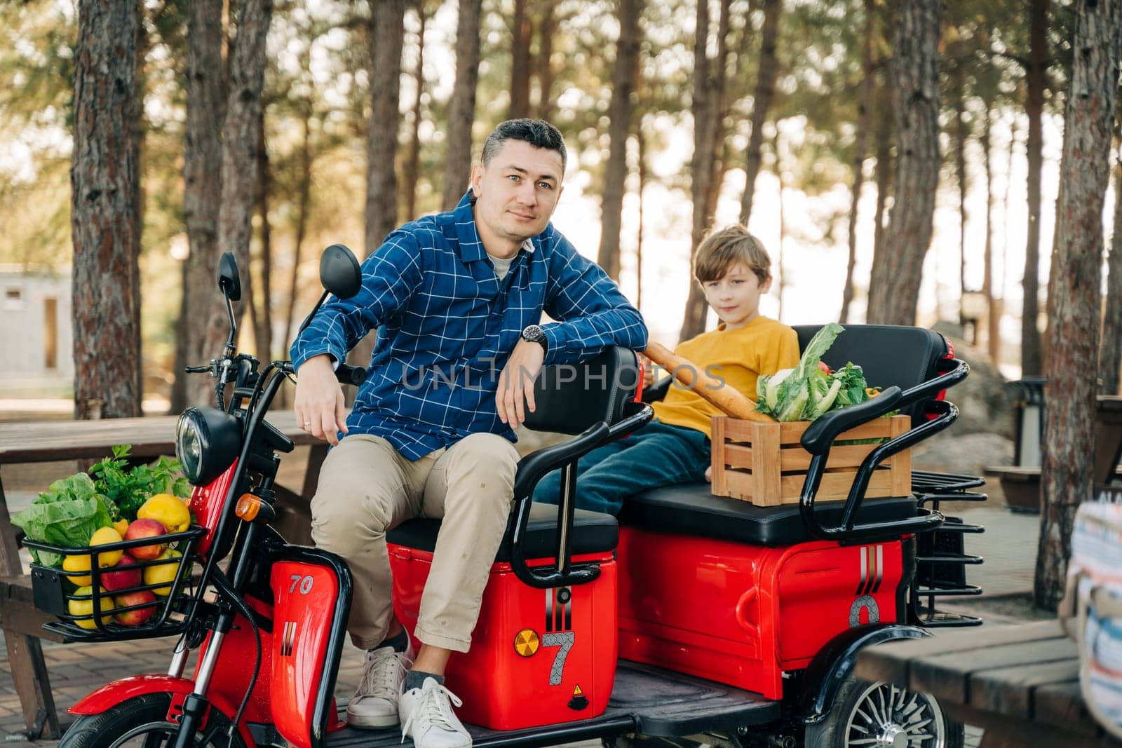 Farmer father and school boy kid delivered wooden crates with vegetables to camp site for picnic. Dad man male and son tourists delivered groceries on electric tricycle vehicle in the forrest. by Ostanina